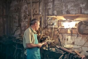 A craftsman focuses on his work in a dimly lit, rustic workshop filled with tools and equipment.