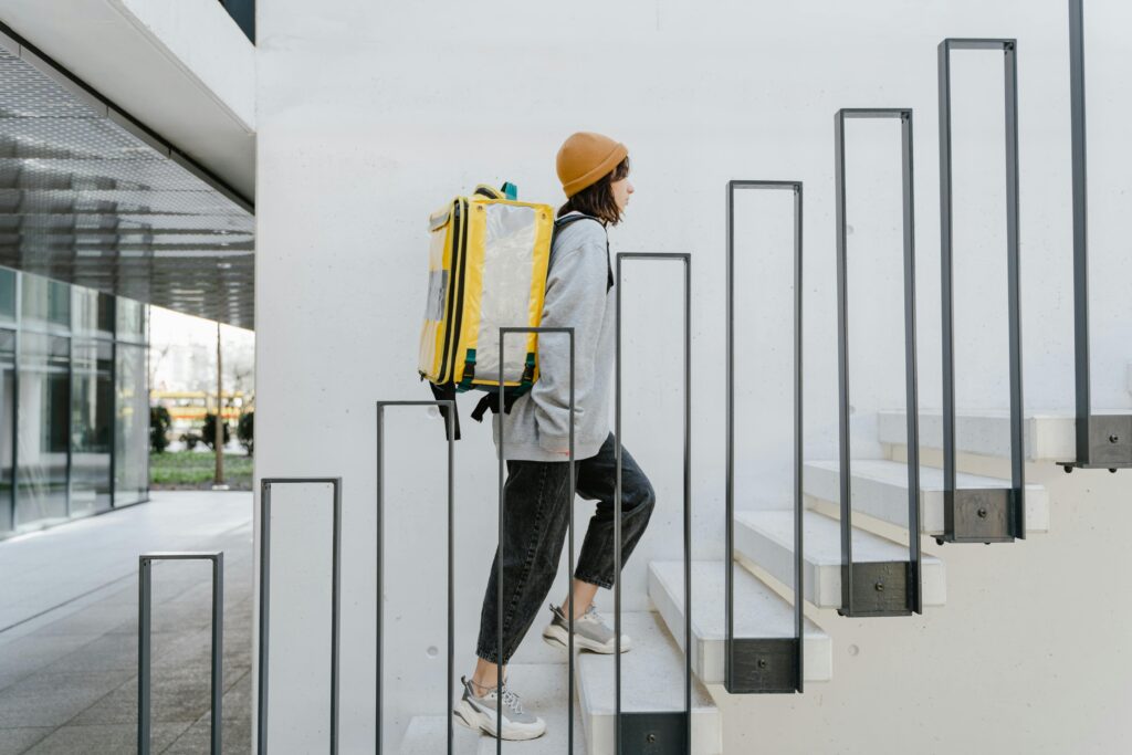 A female courier ascends stairs in an urban setting with a thermal delivery backpack.
